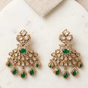 May include: A pair of gold-toned chandelier earrings. Each earring features a central oval emerald-green stone, surrounded by clear, teardrop-shaped and round crystals. The earrings have a fan-like design with dangling emerald-green teardrops.