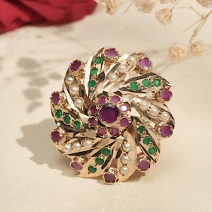 以下が含まれることがあります： 金色のリング。中央に大きな紫色の宝石があり、その周りに小さな紫、緑、白の宝石が配置された花のモチーフ。 リングのデザインは複雑で、詳細なスパイラルパターンです。