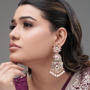 Peut inclure: Boucles d'oreilles pendantes ornées avec un motif géométrique. Les boucles d'oreilles présentent une combinaison de pierres précieuses rouges, vertes et bleues, avec de petites perles blanches suspendues en bas. Les boucles d'oreilles sont serties dans un métal doré.