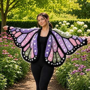 May include: A crochet cardigan designed to resemble butterfly wings, featuring a black base with panels of light pink, lavender, and sage green yarn. The garment is accented with small white flower motifs along the edges and wing segments.