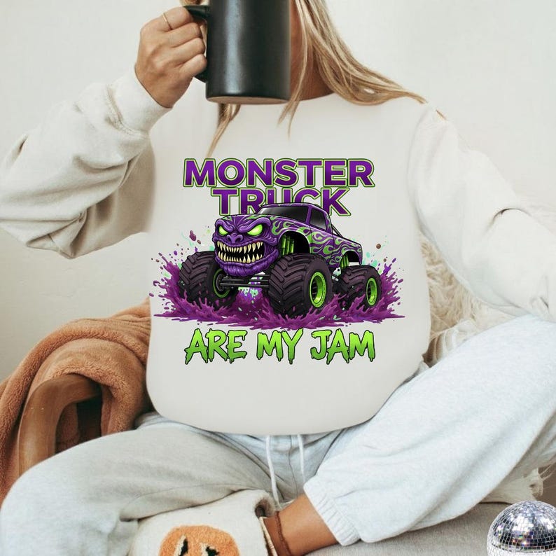 May include: White sweatshirt featuring a purple monster truck graphic with green accents and the text "MONSTER TRUCK ARE MY JAM". The design includes a monster truck with a menacing face and large tires.