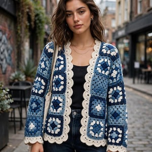 Può includere: Un cardigan a maniche lunghe aperto sul davanti, realizzato con motivi quadrati all'uncinetto in varie tonalità di blu e bianco. Il capo presenta un bordo smerlato color crema lungo l'apertura frontale, lo scollo e i polsini, indossato sopra un top nero.