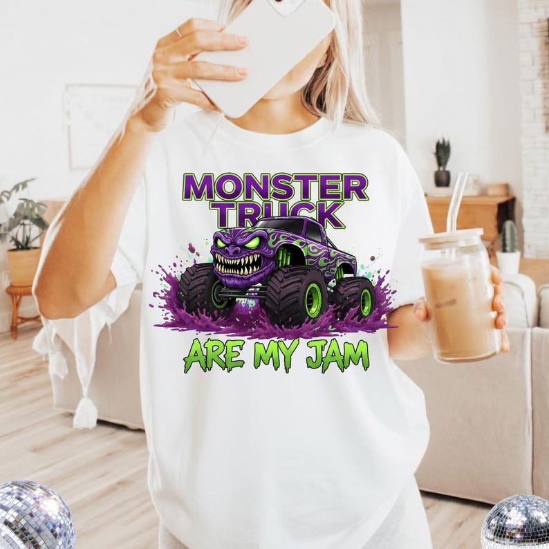 May include: White t-shirt featuring a purple monster truck graphic with green accents and the text "MONSTER TRUCK ARE MY JAM". The design includes a monster truck with a menacing face and large tires.