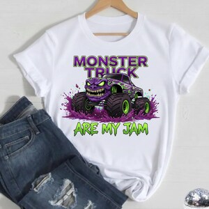 May include: White t-shirt featuring a purple monster truck graphic with green accents and the text "MONSTER TRUCK ARE MY JAM". The design includes a monster truck with a menacing face and large tires.