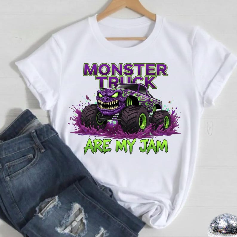 May include: White t-shirt featuring a purple monster truck graphic with green accents and the text "MONSTER TRUCK ARE MY JAM". The design includes a monster truck with a menacing face and large tires.