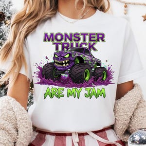 May include: White t-shirt featuring a purple monster truck graphic with green accents and the text "MONSTER TRUCK ARE MY JAM". The monster truck has a menacing face and large tires.