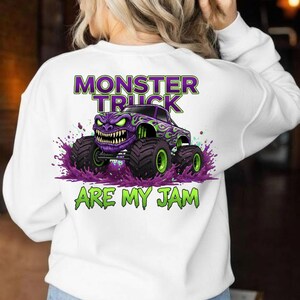 May include: White sweatshirt featuring a purple monster truck graphic with green and purple accents. The text "MONSTER TRUCK ARE MY JAM" is printed above and below the truck design. The truck has large black tires with green rims.