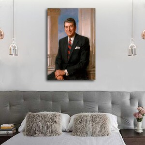 Puede incluir: Retrato enmarcado de un hombre con traje de raya diplom&aacute;tica negro, camisa blanca y corbata a rayas rojas. El retrato est&aacute; ambientado sobre un fondo de columnas cl&aacute;sicas y cielo azul. El hombre est&aacute; sentado, sonriendo, con las manos entrelazadas.