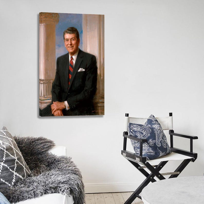 Puede incluir: Un retrato enmarcado de un hombre con un traje a rayas oscuras y una corbata a rayas rojas y azules. El retrato est&aacute; colgado en una pared blanca. Una silla de director con un coj&iacute;n azul estampado est&aacute; en primer plano.