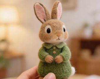 May include: A handcrafted, brown bunny figurine with pink-lined ears and a green knitted dress. The bunny has black eyes and a white tail. The figurine is made of soft, textured material, giving it a charming, handmade appearance. A delightful, whimsical decorative item.