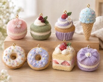 May include: A collection of eight miniature felt food charms including a pink macaron with a flower, a green macaron with berries, a purple cupcake, a blue ice cream cone, two donuts with sprinkles, a strawberry cake, and a purple bow macaron.