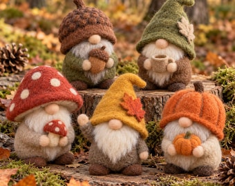 May include: Five needle-felted gnomes featuring autumn themes. One wears an acorn cap, one a green hat with a leaf, one a red mushroom cap, one a yellow hat with a leaf, and one a pumpkin hat. Each gnome has a white beard and holds a small item.