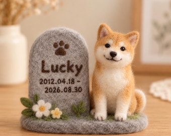 May include: A needle-felted Shiba Inu dog figurine sitting next to a gray felt tombstone. The tombstone features a brown paw print, the name Lucky, and the dates 2012.04.18 - 2026.08.30. Small white and yellow felt flowers decorate the base.