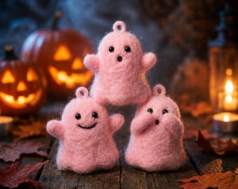 May include: Three small, fuzzy, light pink felt ghost ornaments with loops at the top. Each ghost has two black bead eyes and a unique stitched mouth expression: one with an open O-shape, one with a wide smile, and one with a small surprised mouth.