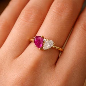 Può includere: Un anello d'oro con un rubino a forma di pera e un diamante a forma di pera, accentuati da piccoli diamanti. L'anello ha una sottile fascia d'oro. Le pietre preziose sono incastonate vicine, creando un design unico.