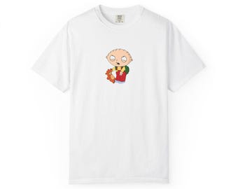 May include: White t-shirt featuring a cartoon image of Stewie Griffin from Family Guy, holding a teddy bear. The character is depicted in his signature red overalls, green shirt, and yellow hair. The shirt has a crew neck and short sleeves.