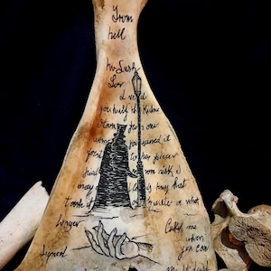 Può includere: Un'opera d'arte a forma di osso con testo scritto a mano e un'illustrazione nera di una figura sotto un lampione. Il testo include frasi come "From hell" e "Catch me when you can". L'opera ha un'estetica gotica vintage.