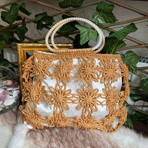 May include: A tan-colored, open-weave handbag with a white satin lining. The bag features a floral design and a beaded handle. The bag is sitting on a faux fur surface.