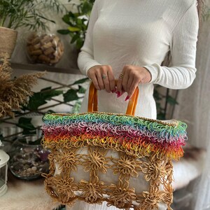 Puede incluir: Un bolso tote hecho a mano con una parte superior de color arco&iacute;ris y un dise&ntilde;o floral. El bolso tiene un interior blanco y asas marrones. El bolso est&aacute; hecho de materiales tejidos.