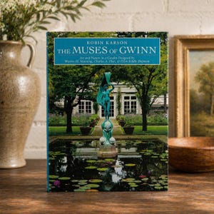 Könnte beinhalten: Ein Buch mit dem Titel "The Muses of Gwinn" von Robin Karson. Das Cover zeigt ein teal- und grünes Bild eines Gartens mit einer Statue in einem Teich. Das Buch liegt auf einer Holzoberfläche.