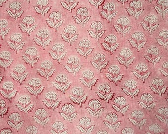 Op de afbeelding: Close-up van een roze stof met een herhalend bloemenpatroon. De bloemen zijn wit met rode stelen en bladeren. De stof heeft een getextureerde uitstraling, mogelijk gemaakt van katoen of linnen.