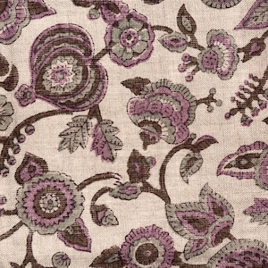 May include: Close-up of a fabric with a floral pattern. The design features stylized flowers and leaves in shades of purple, gray, and brown against a cream-colored background. The fabric has a textured appearance.