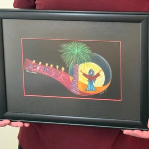May include: A framed artwork featuring a colorful illustration on a black background. The scene depicts a line of figures walking toward a palm tree and a central figure with arms raised inside a yellow circle. The frame is black with a red border.