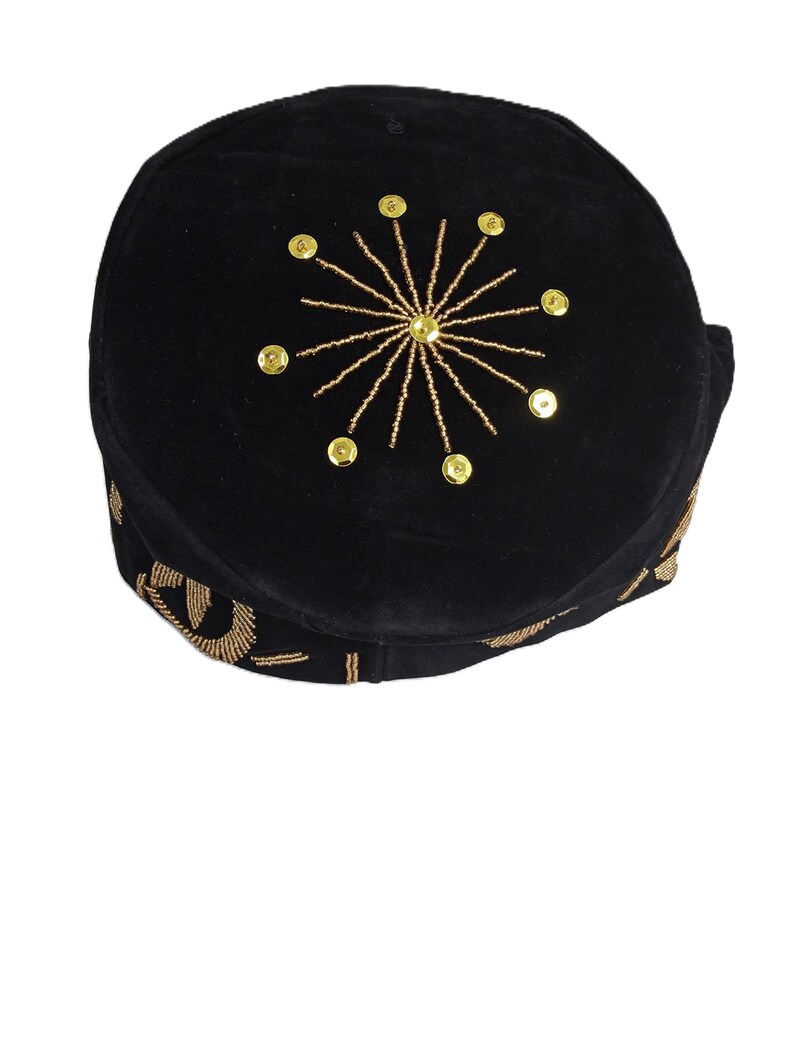 May include: Black velvet cap with gold-colored embellishments. The cap features a sunburst design made of gold beads and sequins on the crown. The brim is also decorated with gold embroidery. This headwear is suitable for special occasions.