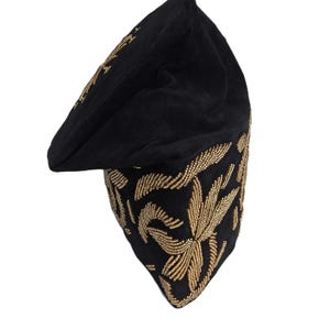 May include: Black beret-style hat with gold-colored floral embroidery. The hat has a rounded crown and a small, flat brim. The gold embroidery is detailed and covers the lower portion of the hat, creating a striking contrast against the black fabric.