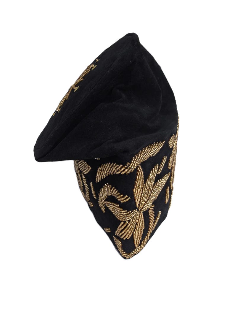 May include: Black beret-style hat with gold-colored floral embroidery. The hat has a rounded crown and a small, flat brim. The gold embroidery is detailed and covers the lower portion of the hat, creating a striking contrast against the black fabric.