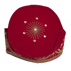 May include: A red velvet hat with gold beaded trim and a gold embroidered starburst design on top. The hat is a traditional style, likely for a special occasion or cultural event.