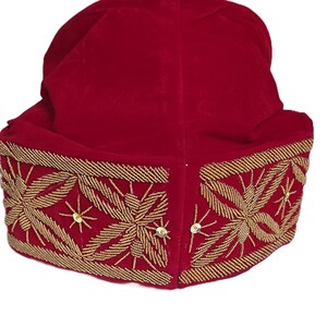 May include: A red velvet hat with gold beaded floral embroidery. The hat features a rounded crown and a wide, embellished brim. The gold embroidery includes star-like accents and small sequins.