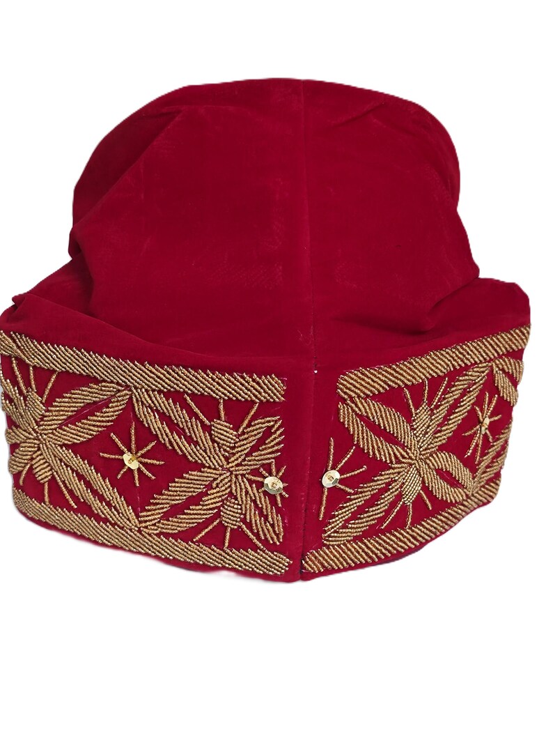 May include: A red velvet hat with gold beaded floral embroidery. The hat features a rounded crown and a wide, embellished brim. The gold embroidery includes star-like accents and small sequins.