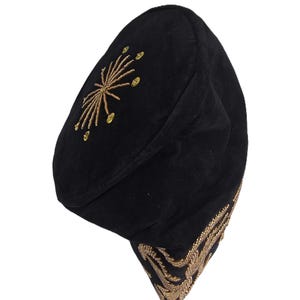 May include: Black beret-style hat with gold embroidered accents. The hat features a starburst design on the crown and ornate detailing along the brim. The hat is made of a soft, dark fabric.