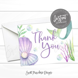 May include: Purple and green mermaid tail thank you card with a pearl and seashells. The card has the text "Thank You" in purple lettering.