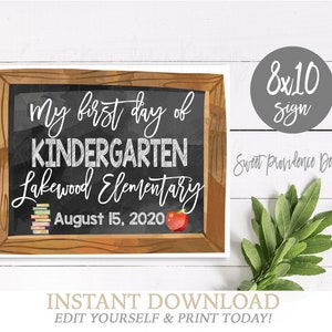 Op de afbeelding: Een rechthoekig bord met een bruine lijst in houtlook en een zwart schoolbord in het midden. De tekst luidt My first day of KINDERGARTEN Lakewood Elementary August 15, 2020. Het bevat een kleine stapel kleurrijke boeken en een rode appel.