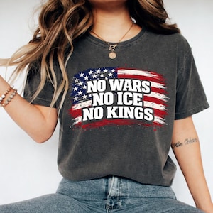 May include: Dark gray t-shirt featuring a distressed American flag design with the text "NO WARS, NO ICE, NO KINGS" in white. The flag design incorporates red and blue colors, creating a patriotic theme.