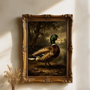Peut inclure: Une impression d'art encadrée représentant un canard colvert debout près d'un étang dans un paysage boisé. Le canard a une tête verte, un corps brun et un bec jaune. L'œuvre est insérée dans un cadre rectangulaire doré de style ancien.
