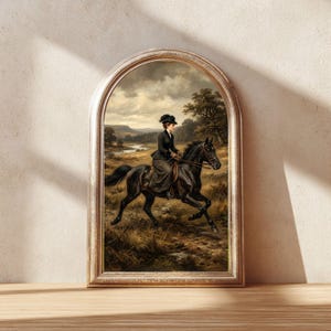 May include: Framed vintage print of a woman riding a black horse through a field. The artwork features a woman in a dark dress and hat, set against a landscape with a river and trees. The frame has a gold finish.