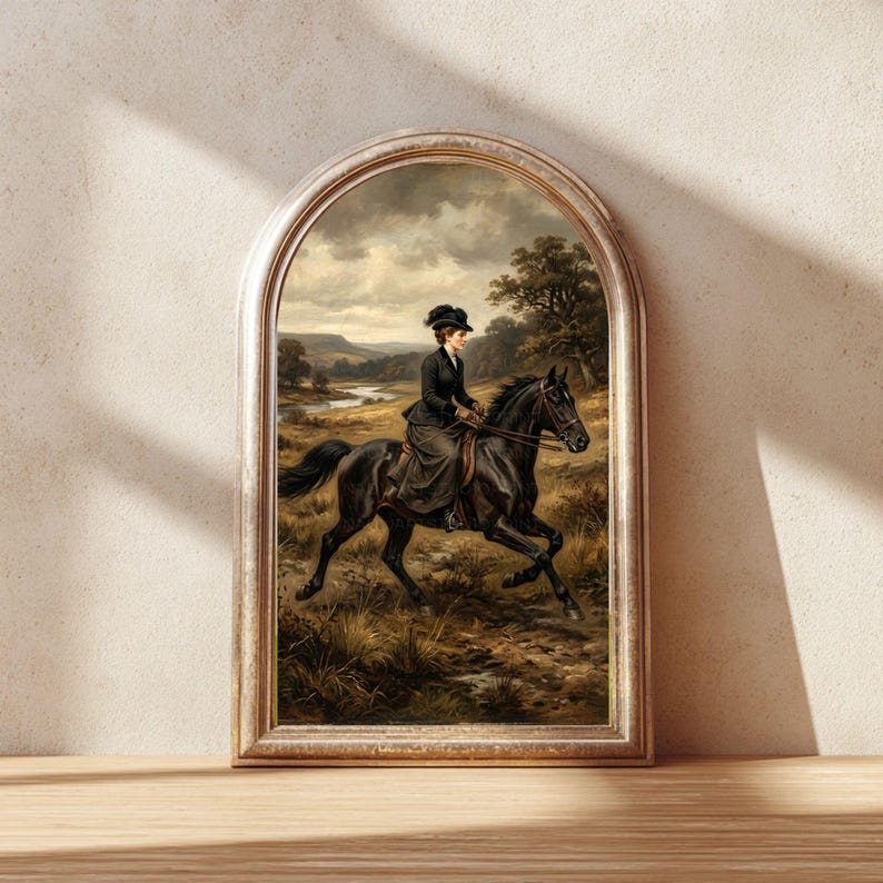 May include: Framed vintage print of a woman riding a black horse through a field. The artwork features a woman in a dark dress and hat, set against a landscape with a river and trees. The frame has a gold finish.