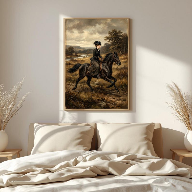 May include: A framed vintage painting depicts a woman riding a black horse across a field. The rider wears a dark dress and hat. The background shows a landscape with a river and trees under a cloudy sky. The artwork is displayed above a bed.
