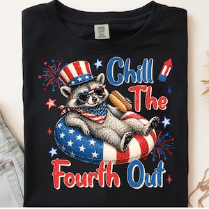 Peut inclure: T-shirt noir avec un dessin d'un raton laveur portant des lunettes de soleil, un chapeau patriotique et un bandana, se relaxant sur un anneau gonflable rouge, blanc et bleu. Le texte "Chill The Fourth Out" est affiché.