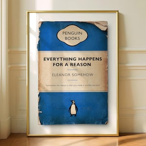 May include: A framed print featuring a vintage-style blue book cover with the text PENGUIN BOOKS, EVERYTHING HAPPENS FOR A REASON, and ELEANOR SOMEHOW. The design includes a small penguin illustration and distressed edges on a gold-colored frame.