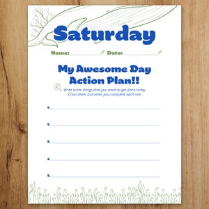 以下が含まれることがあります： 青い「Saturday」の文字、クジラのイラスト、そして「My Awesome Day Action Plan!!」というテキストが特徴の白い紙のプランナー。タスクを書き込むための線と、名前と日付のスペースがあります。