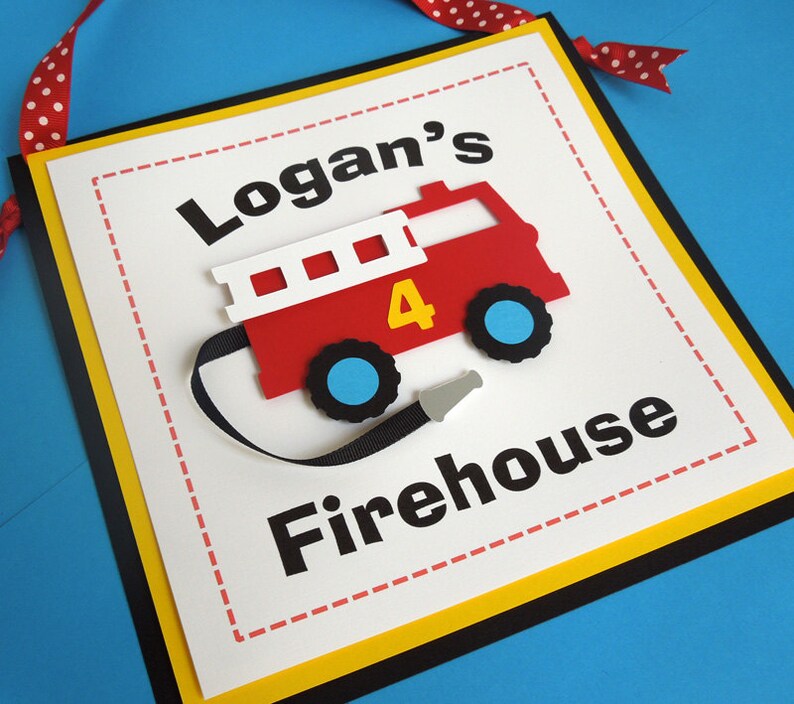 May include: A white sign with a yellow border and black trim. The sign has a red fire truck with a black hose and the words "Logan's Firehouse" in black.