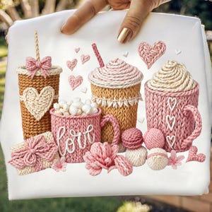 Puede incluir: Tela blanca con una colección de tazas de café, tazas y una caja de regalo de punto, todo en tonos de rosa, beige y marrón. La palabra "amor" está escrita en una taza. También hay corazones y flores decorativas.