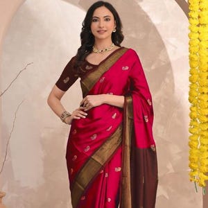 Op de afbeelding: Een levendige magenta sari met gouden en bruine randen. De sari heeft ingewikkelde gouden borduursels en een bijpassende bordeauxrode blouse. De stof valt elegant. Een traditioneel Indiaas kledingstuk, perfect voor speciale gelegenheden.