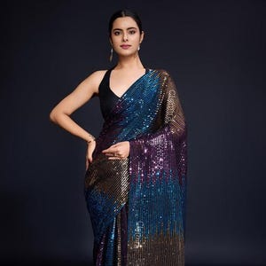 May include: A woman wearing a black halter top and a sequined saree. The saree features a gradient of colors, including blue, purple, and gold. The fabric is covered in small, reflective sequins.