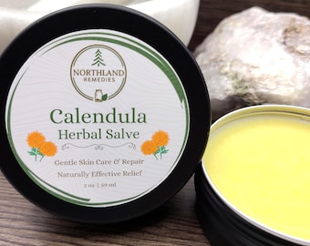 May include: A black tin of Calendula Herbal Salve with a white and green label. The label reads "Northland Remedies" and "Gentle Skin Care & Repair." The salve is yellow and the tin is 2 oz / 59 ml.
