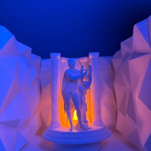 Könnte beinhalten: Eine weiße, 3D-gedruckte Skulptur einer klassischen Figur, die eine Leier hält, beleuchtet von einem orangefarbenen Licht. Die Skulptur wird von zwei weißen Säulen flankiert und vor einem blauen Hintergrund platziert. Geometrische, weiße Strukturen rahmen die Szene ein.